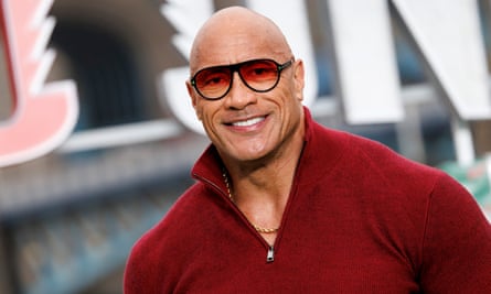 a man wearing a red quarter-zip sweater and sunglasses smiles 