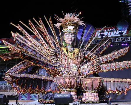 An embellished statue of a person wearing features and a headdress playing the drums