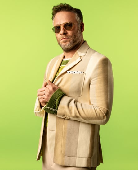 Actor Seth Rogen, in sunglasses and cream and brown jacket striped jacket, against bright green background 