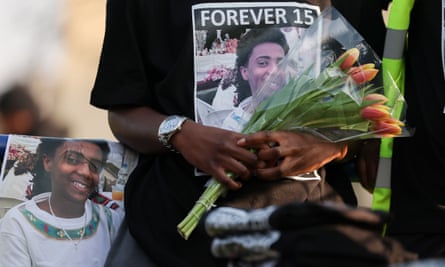 Close-up of a mourner holding tulips and wearing a T-shirt with a picture of Amen on it, with the words 'Forever 15'