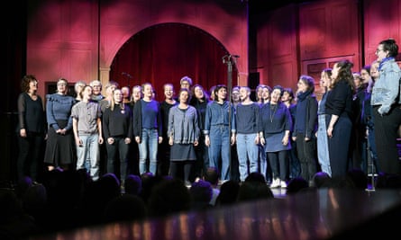 Women in the choir sing on stage as an audience looks on