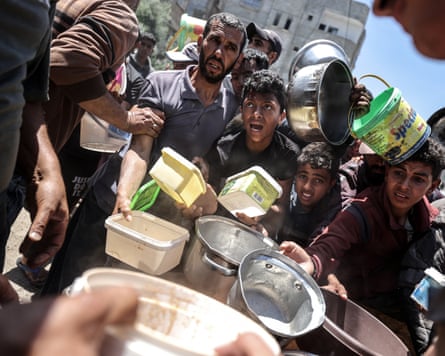 A crowd of people holding out containers for food