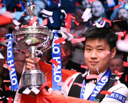 Zhao Xintong holding aloft a silver trophy under falling ticker tape