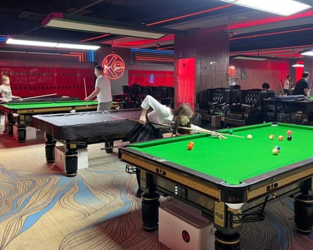 A woman is playing a shot at the nearest table and people are standing around other tables